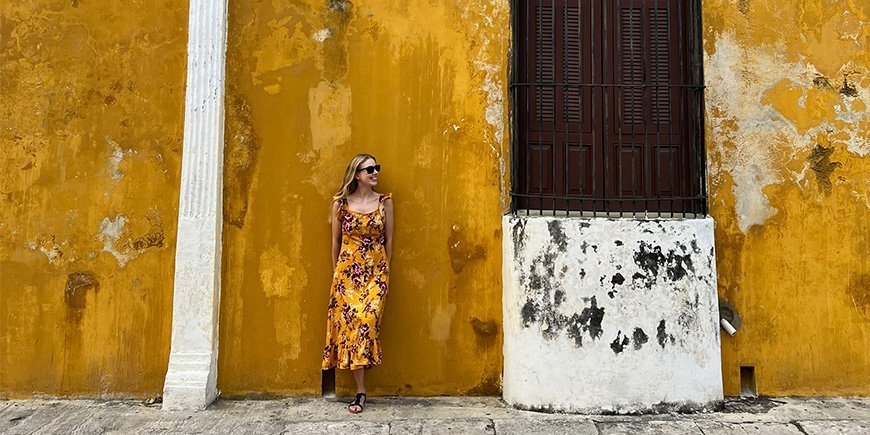 Woman in orange dress leaning against orange wall in Izamal, Mexico.
