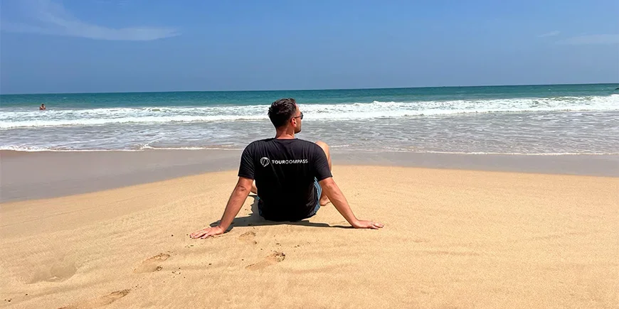 A man in a TourCompass T-shirt sitting on the beach in Mirissa, Sri Lanka