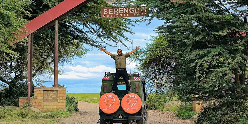 Safari guide Madeal standing in front of the Serengeti sign on TourCompass safari jeeps