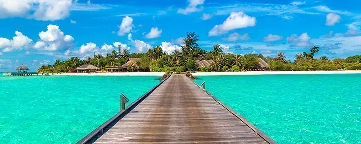 Water villas (bungalows) and wooden bridge on tropical beach in Maldives on a summer day